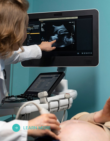 A radiology technician moves a probe over a pregnant patient’s belly while pointing to an ultrasound screen