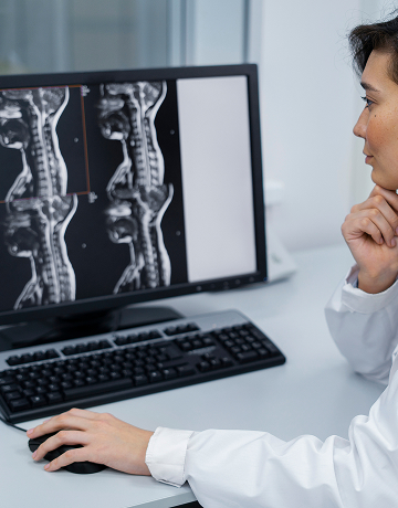 A radiologist sits in their office at a diagnostic imaging center and looks at MRI scans on their computer