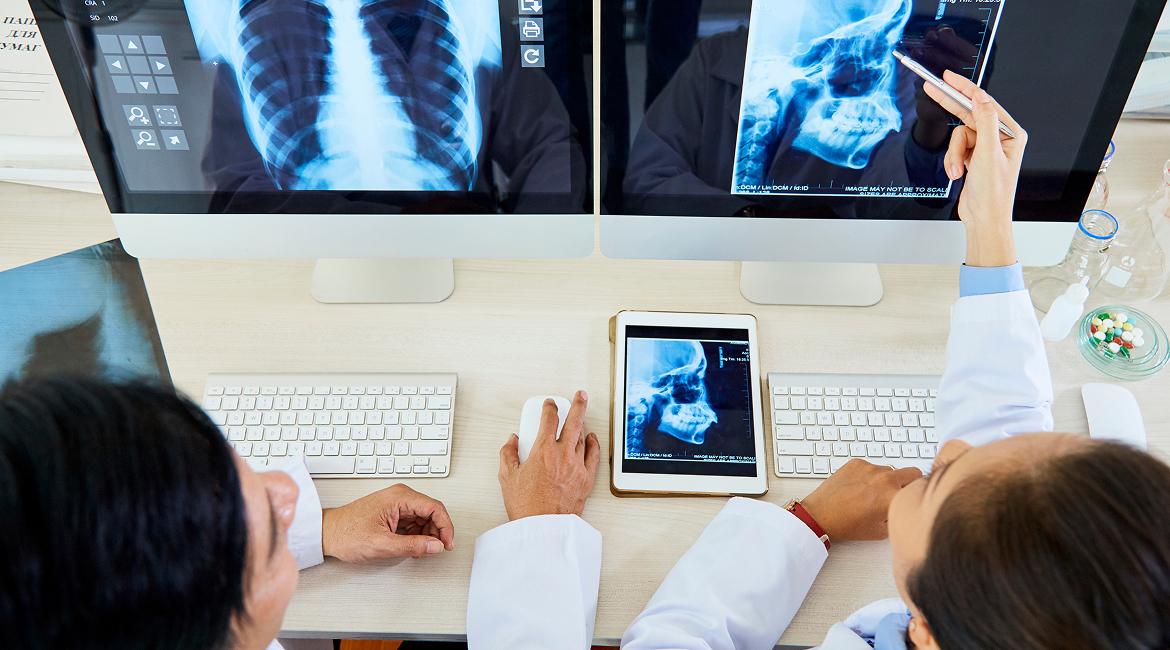 Radiologists sit at a desk, look at X-rays on their computers, and discuss their patient’s diagnosis