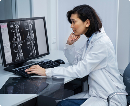 Un radiólogo se sienta en un escritorio y mira exploraciones de una máquina de tomografía computarizada en su computadora