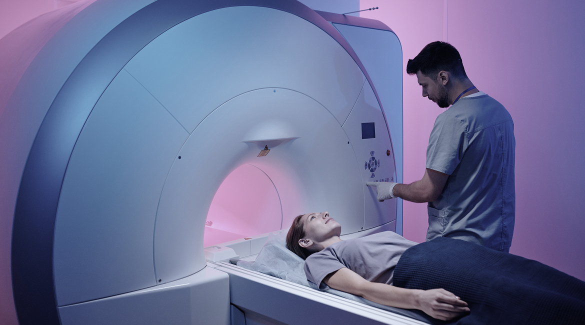A technician pushes buttons on an MRI machine while a patient lies down on a sliding table for an MRI scan