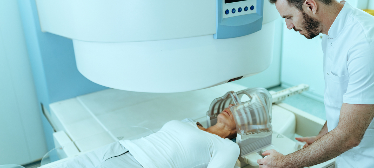 A radiology technician prepares an MRI machine for a patient who’s lying down and waiting for a brain MRI scan