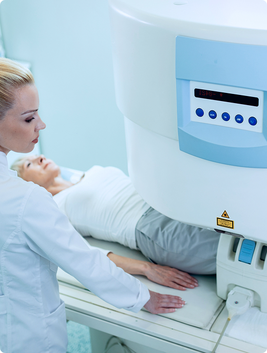 A patient gets an MRI scan of their knee while a radiology technician stands by the MRI machine at an imaging center