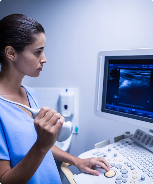 Un técnico de radiología presiona botones en una máquina de ultrasonido mientras sostiene una sonda y mira una pantalla de ultrasonido