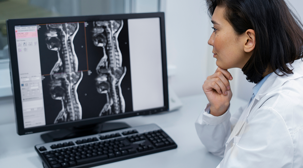 A radiologist sits in their office at a diagnostic imaging center and looks at bone density scans on their computer