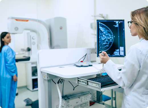 Un radiólogo observa los resultados de una mamografía mientras una paciente se encuentra frente a una máquina de mamografía en el fondo