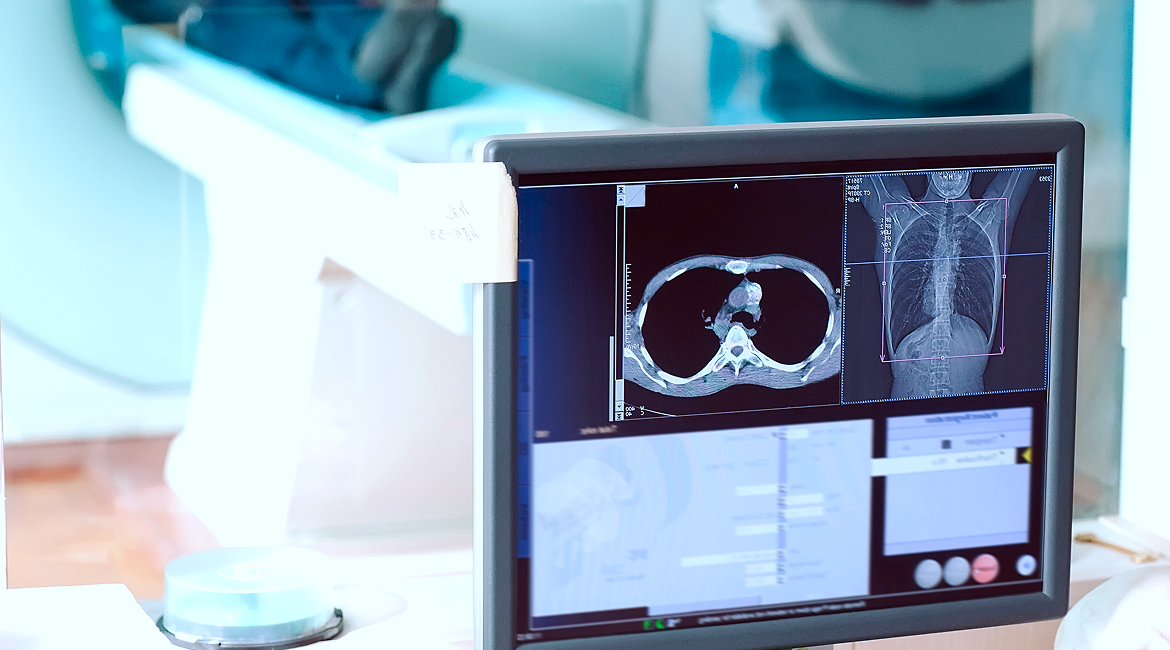 A computer screen shows the live results of a diagnostic test while a patient moves through an MRI machine in the next room