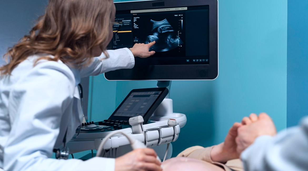 A radiologist moves a probe over a pregnant patient’s belly while pointing to an ultrasound screen