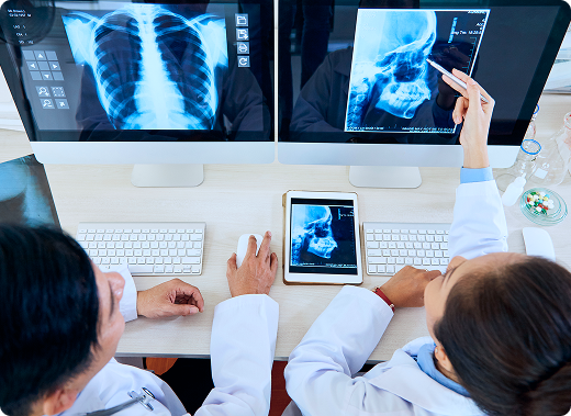 X-rays-content Two radiologists sit at a desk, look at X-rays on their computers, and discuss their patient’s diagnosis
